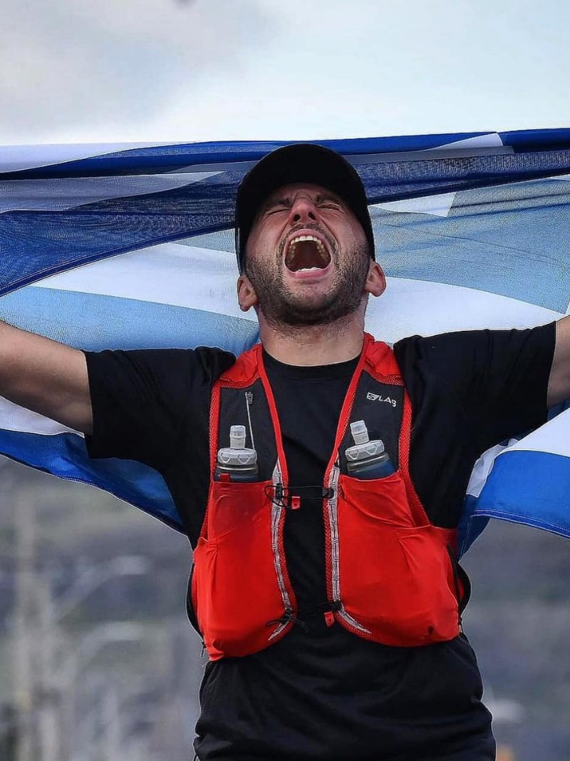 Aris Myrkos, Head of Sport Physiology at DVOTION Labs, finishing a race holding the Greek flag overhead