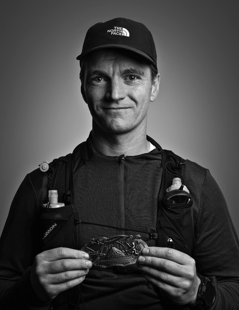 Jacob Lockhart Lister, Health & Performance Coach at DVOTION Labs, wearing a running vest and holding a race buckle